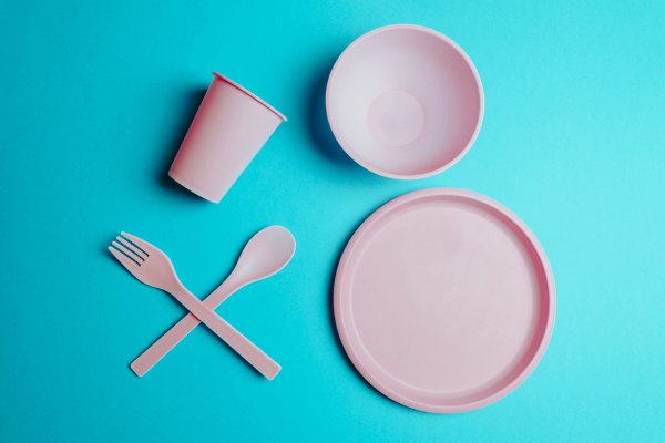 image with plastic tableware alt text: Image of a light pink plastic products like plate, bowl, fork, knife, and a cup on a teal background. This brings to mind the question where melamine is the same as plastic and what are the dangers of melamine contamination and acute melamine poisoning? We know the health concerns but what causes increased risk of ailments like form kidney stones