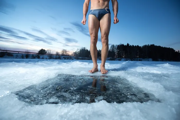 Cryotherapy for brown fat production. Man in bathing suit standing in front of whole in frozen lake,