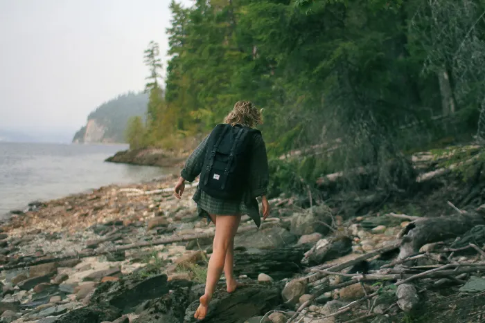 Image of woman walking along a rocky beach on a cloud covered day. Wheatgrass enthusiasts love the outdoors!