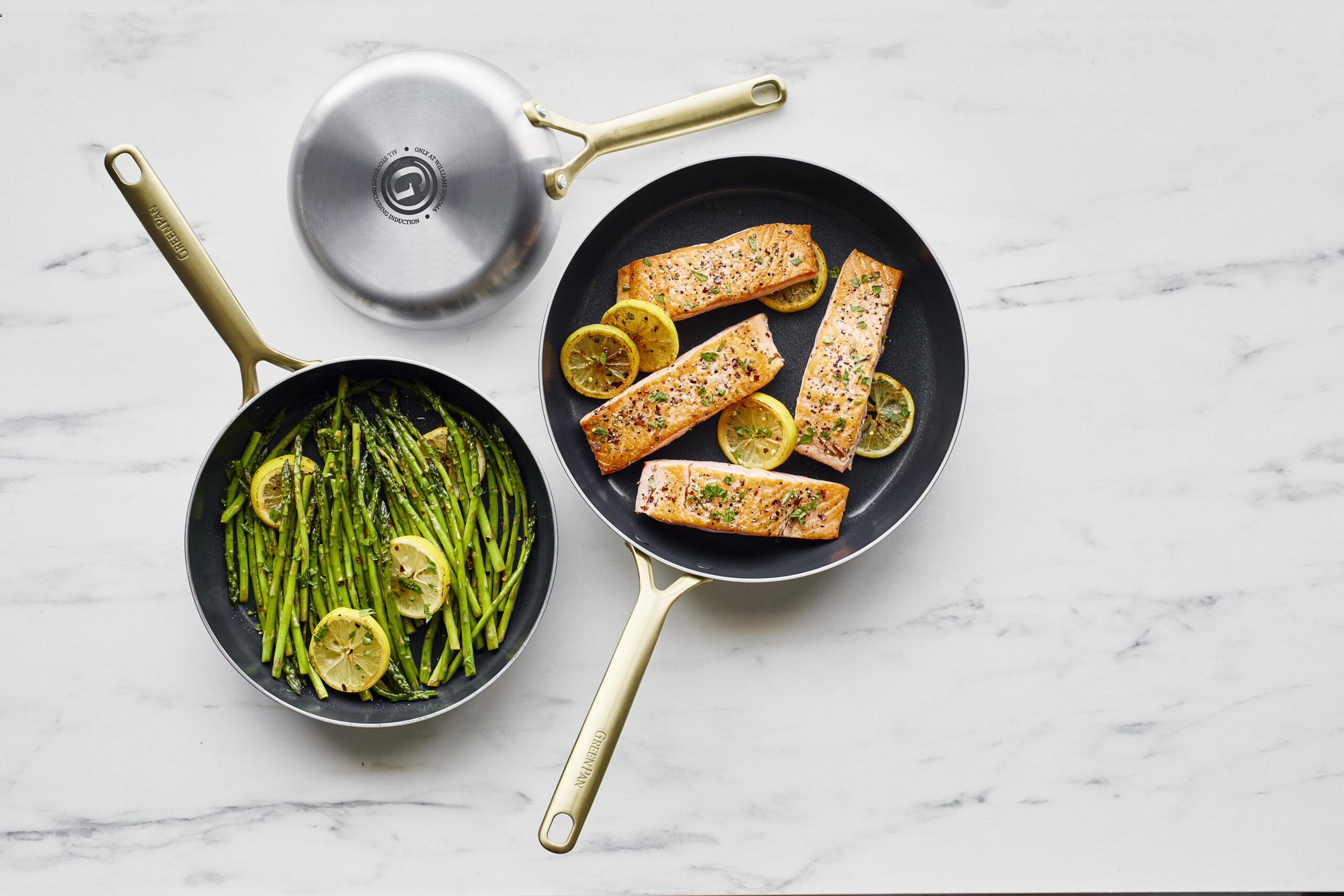 Image of 3 GreenPan GP5 stainless steel pans with champagne handles, one overturned to show off the finish and two filled with food (salmon and asparagus) w/an overhead view.