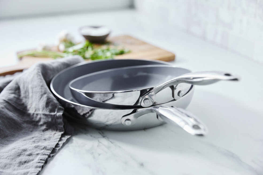 image of 2 GreenPan Valencia Pro new stainless steel pans stacked on a counter with a cutting board in the background.