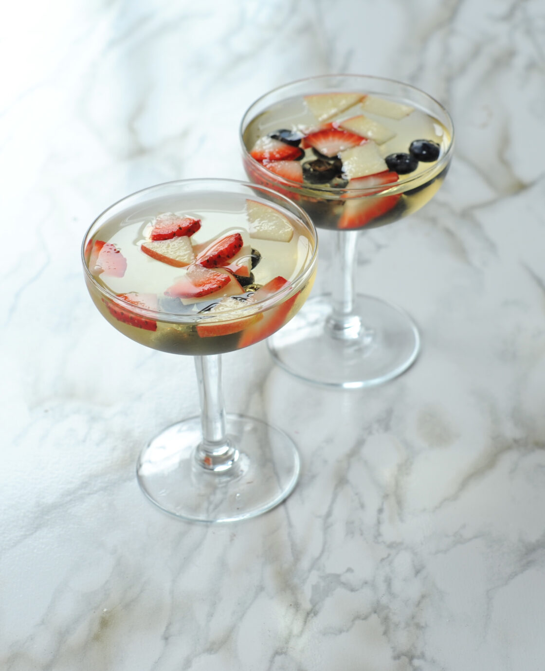 Image of white wine spritzer sangria in two wine glasses with fresh berries. Here's how to make sangria.