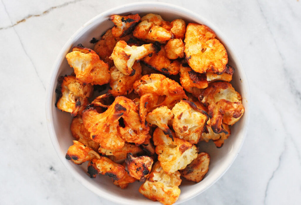 Image of cauliflower hot wings recipe served in a white bowl on a white marble conter.