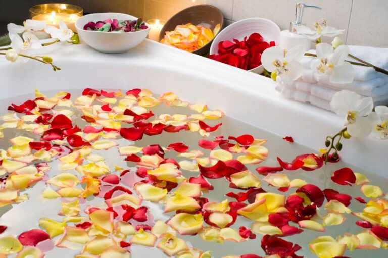 Image of a relaxing bath with rose petals sprinkled around and bowls filled with more alongside, as well as candles for a soothing bath with Epsom salt bath benefits.