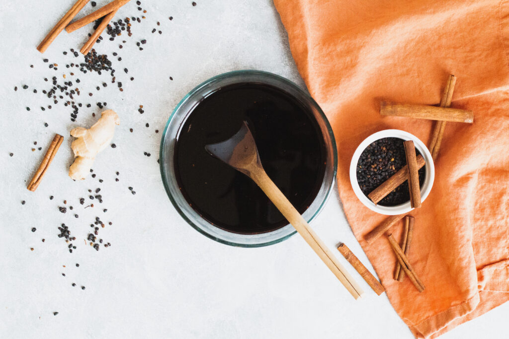 Image of Homemade elderberry syrup recipe for colds and flus in a mason jar with orange towel and cinnamon sticks.