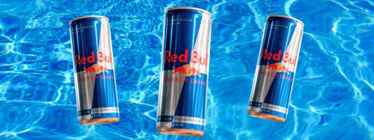 Image of 3 cans of Red Bull with a blue water background showcasing Red Bull ingredients but you'll want to know, are they safe to drink?