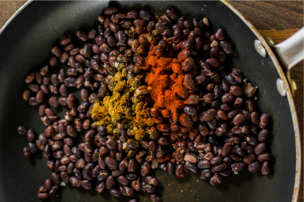 Image of black beans with spices in a black nonstick pan for vegetarian burrito bowls with veg