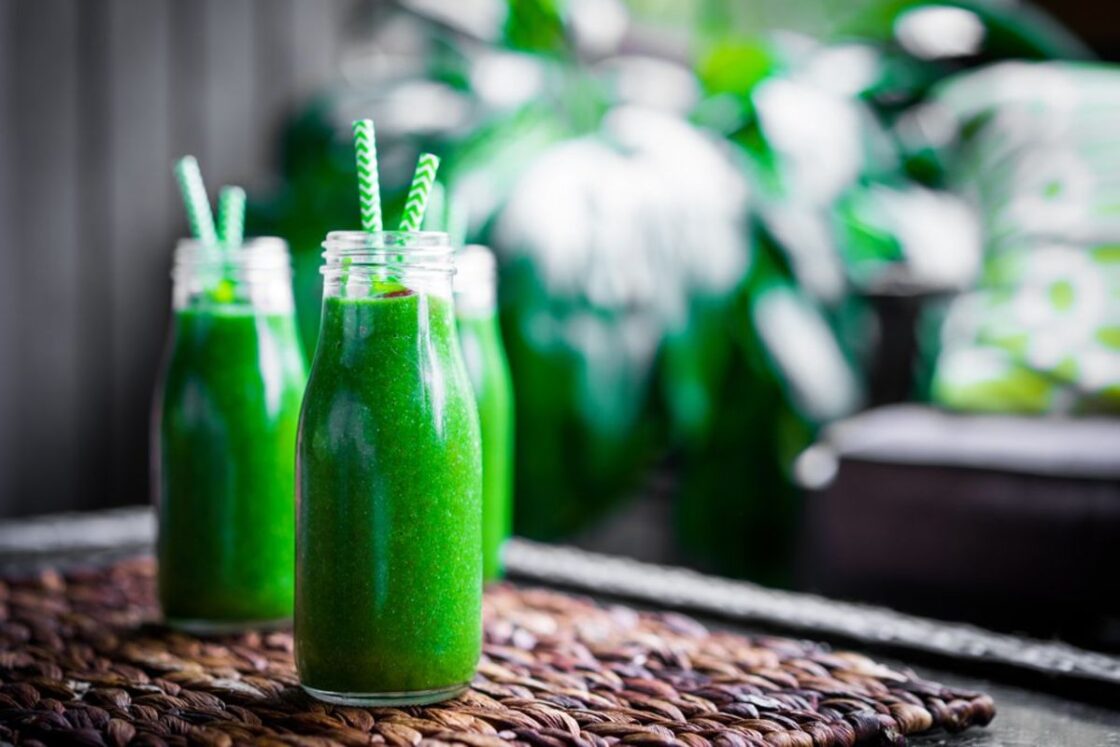 Image of wheatgrass smoothie in mini glass milk jugs with green and white striped straws.