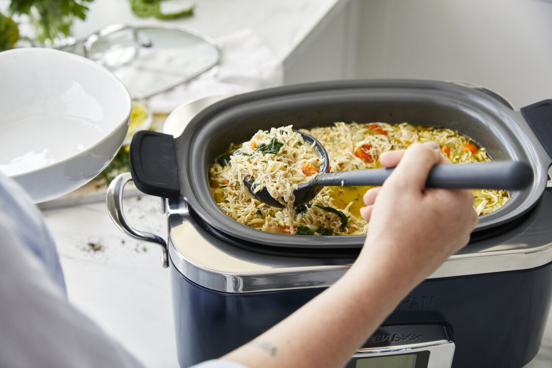 Image of GreenPan Slow Cooker from above with an hand holding a ladle and scooping our Lemon Chicken Orzo Soup that comes in the Slow Cooker recipe book that comes with each purchase.