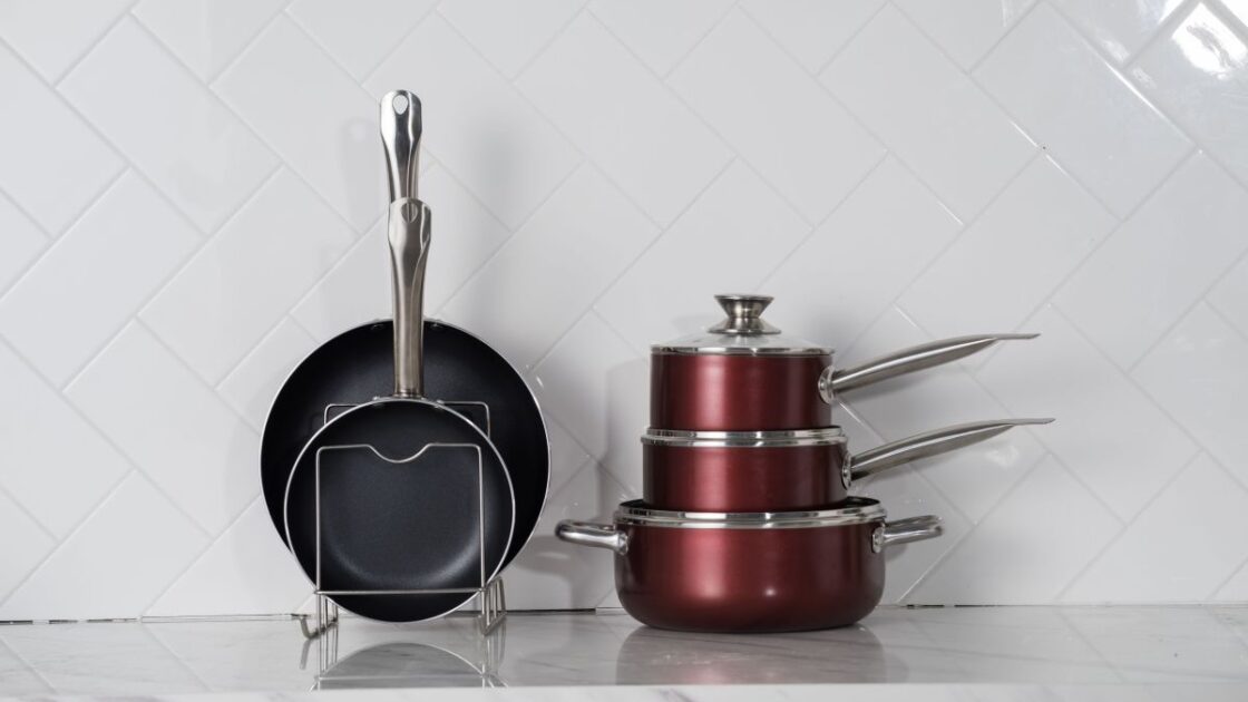 Image of PTFE-free, nonstick, nontoxic cookware stacked on a white marble counter with white tile backsplash for comparison for a Caraway Cookware review