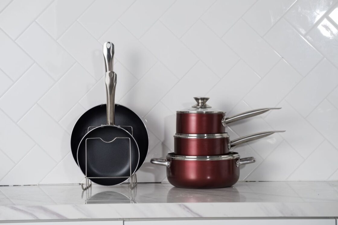 Image of PTFE-free, nonstick, nontoxic cookware stacked on a white marble counter with white tile backsplash for comparison for a Caraway Cookware review