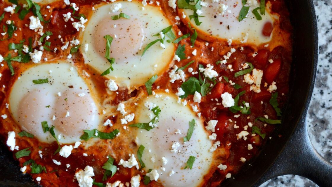 image of Shakshuka recipe, poached eggs in tomato sauce in a cast iron pan on a granite countertop