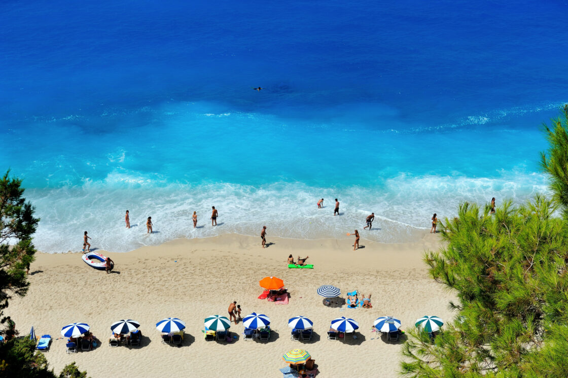 Image of a beach scene with blue and white striped umbrellas and beach goers on a gorgeous day illustrating what you might visualize for you perfect life.