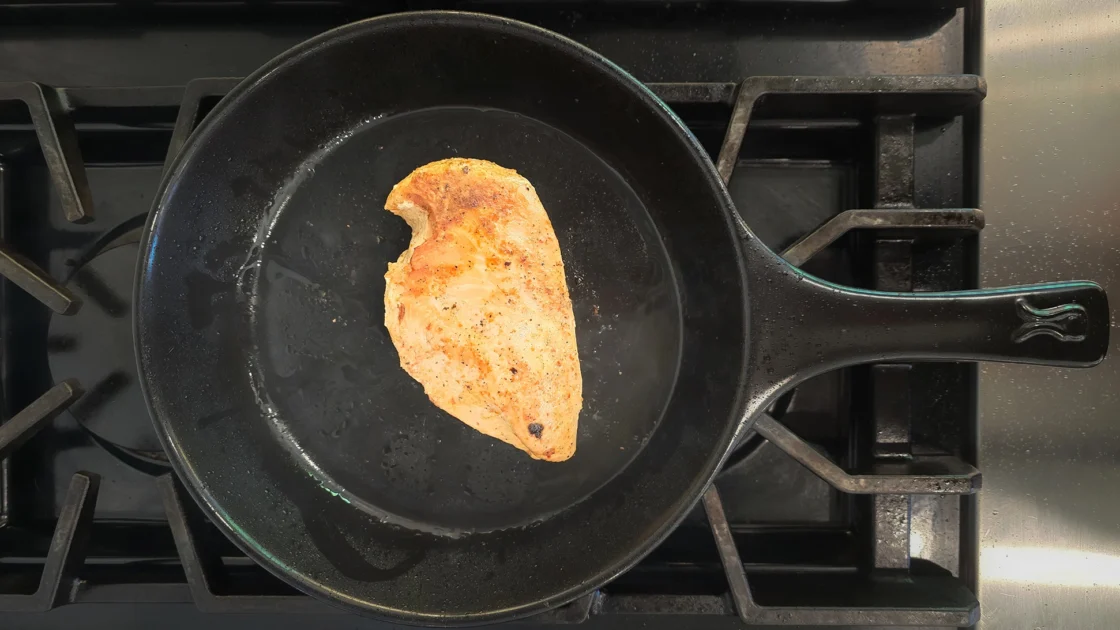 Overhead image of a non-toxic ceramic black skillet with a single chicken breast seared to a golden brown.