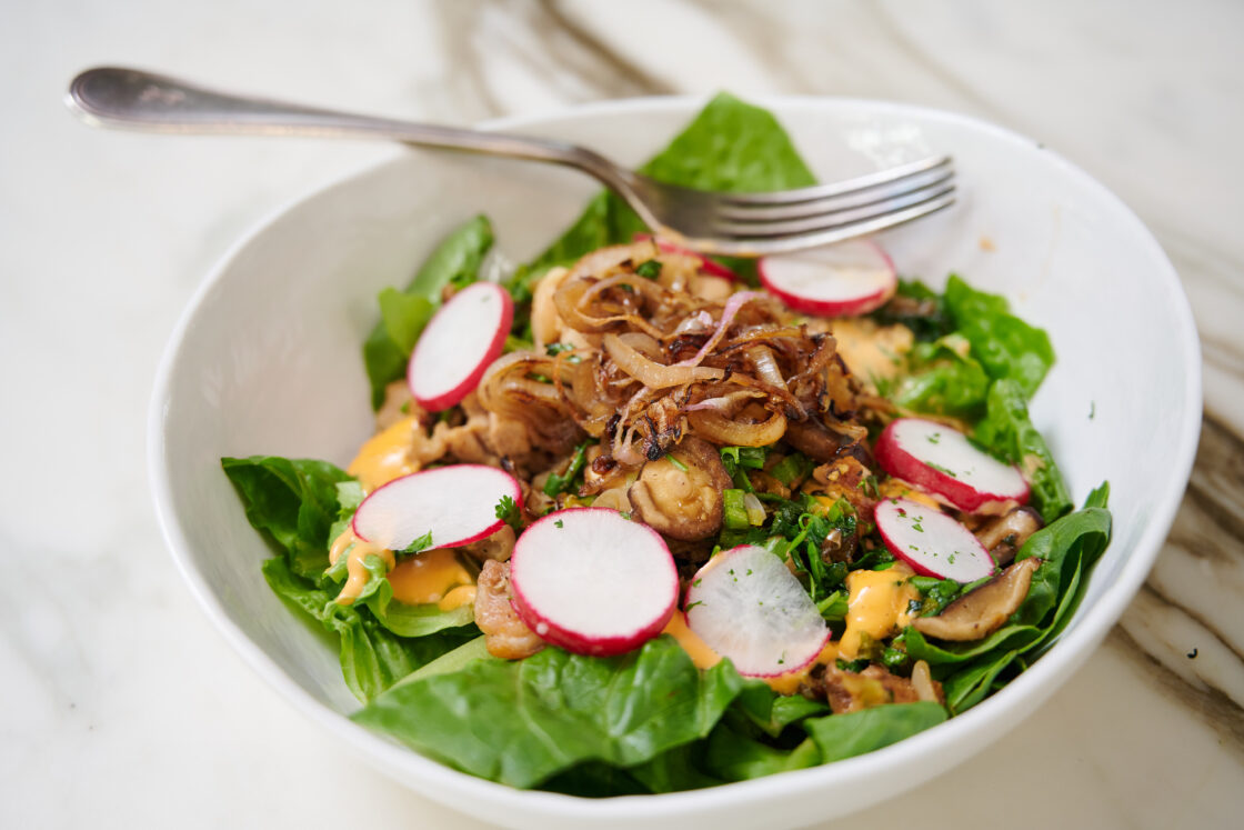 Image of a white chicken bowl recipe filled with romaine lettuce, sauteed chicken and shiitake mushrooms, crispy shallots, and sliced radishes.
