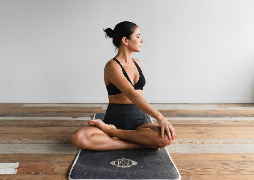 Image of a woman sitting on a black yoga mat with her legs crossed and her eyes closed as she twists to the side in a relaxing stretch.