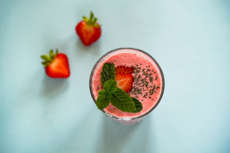 Image of a pink smoothie in a glass, topped with strawberries, greens, and chia seeds. 