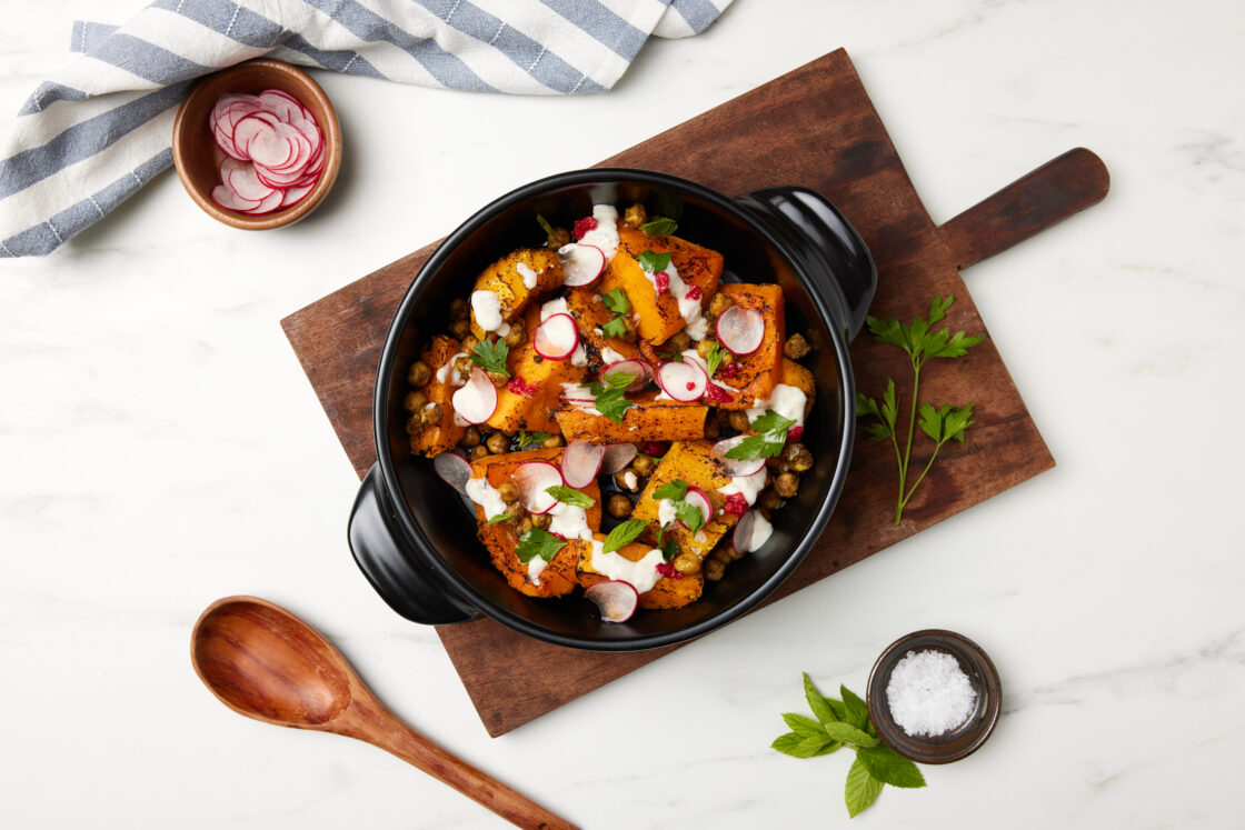 Image of a non toxic ceramic cookware with natural nonstick pure ceramic pan (sauce pans) with roasted vegetables and a drizzle of white cause on a wood cutting board and a white counter with a sprig of parsley off to the side of this sacred fine chinaware.