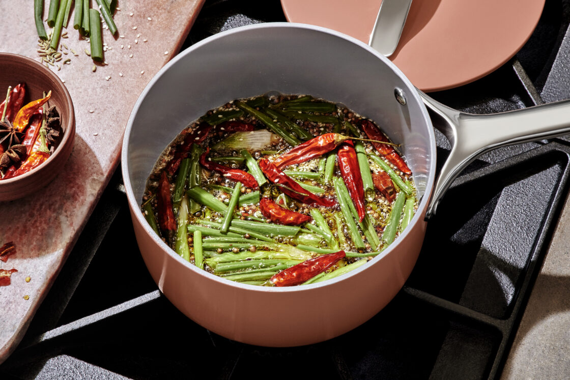 Image of a saucepan with  red chilis, green onions, and soy sauce. The pan in a pretty pink color and it's being used for a Caraway pans review where a chef tests Caraway Cookware Sets