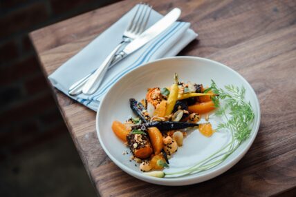 Image of a plate of carrots and orange segments artfully plated on a wood table with a folded cloth napkin with silverware. Least Expensive Fruits and Veggies, Fruits and Vegetables, Unsplash