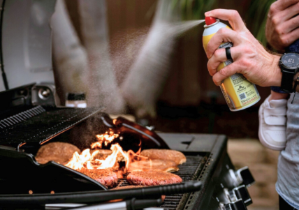 Image of someone spraying cooking oil spray onto a grill with a few burger patties.