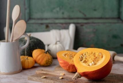 An heirloom pumpkin on a table, cut in half with the pumpkin seeds exposed. Several other pumpkins sit behind it in a seasonal display.