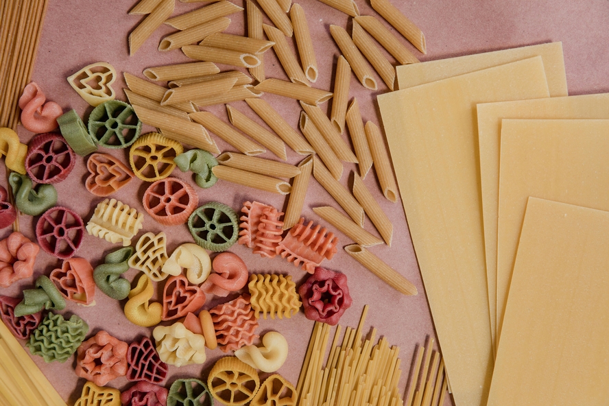 Image of a flat lay of various dry pasta noodles, from colorful shapes to penne and lasagna sheets for easy lasagna soup recipes