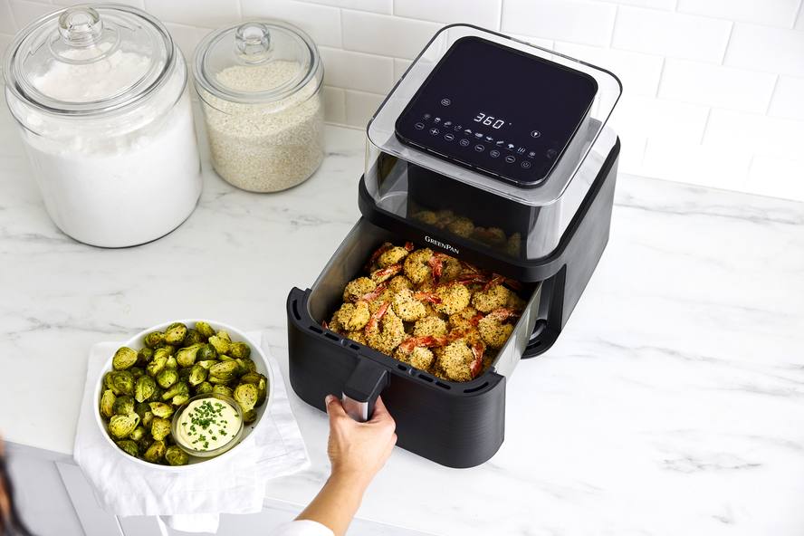 GreenPan Bistro XL Clear View Air Fryer with a hand opening the oven drawer to reveal air fried breaded shrimp. A bowl of brussels sprouts sits on the side.