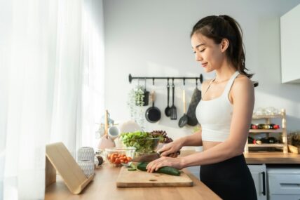 Image of a woman in a kitchen standing at the counter chopping some vegetables on a cutting board.