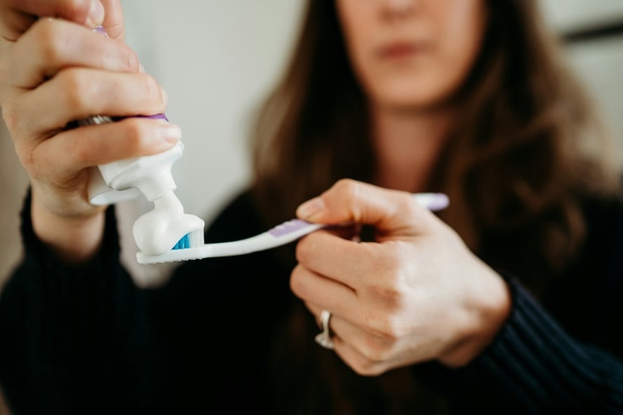 An image of a woman holding a toothbrush and squeezing a generous amount of toothpaste onto its head.