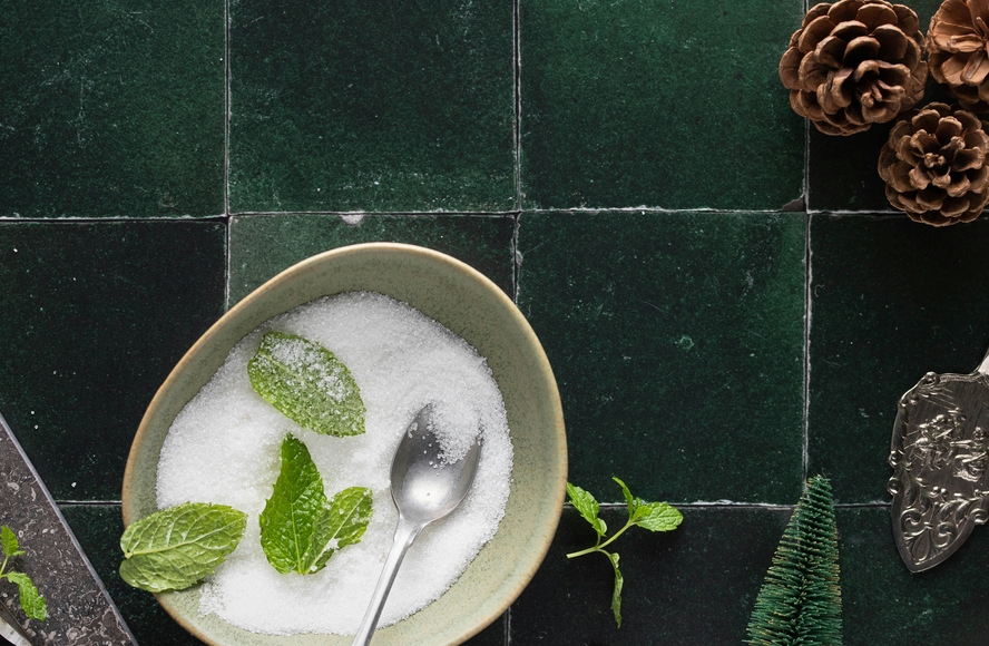 Image of a bowl of white table sugar on a green background, with mint and winter decorations.