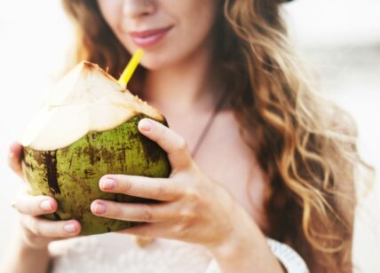 Image of a woman drinking coconut water, which registered dietitian Staci Gulbin recommends as the best hangover remedy.