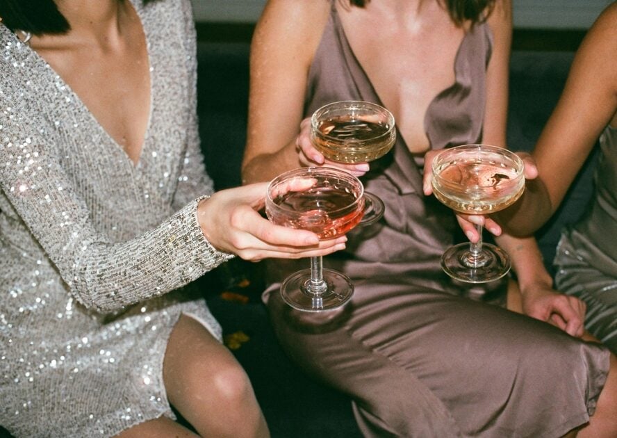 Image of three women in dresses clinking glasses of champagne in a cheers.