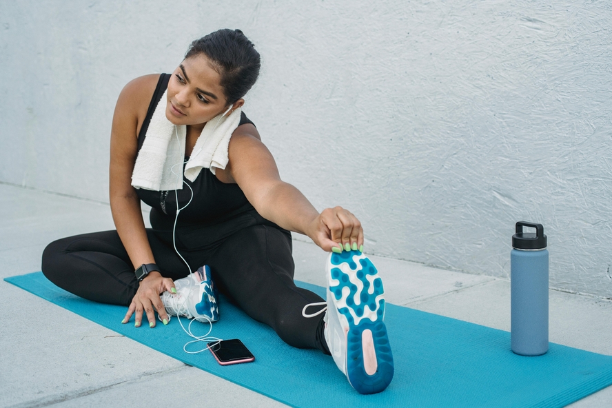 Image of a young woman sitting on a blue yoga mat with one leg extended as she stretches. When it comes to coconut water vs. sports drinks for exercise like yoga, coconut water is the ideal choice.