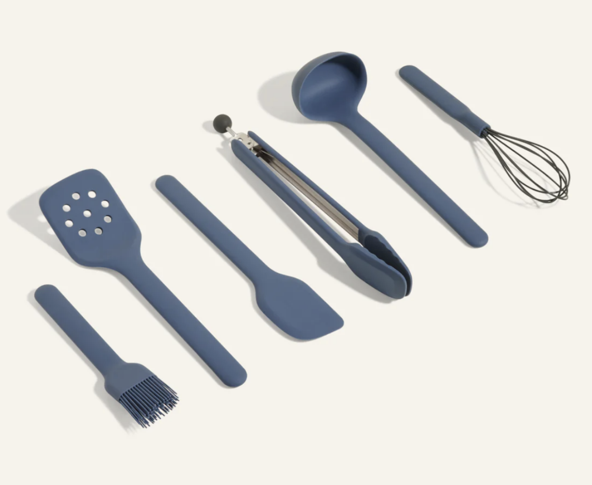 Image of a five-piece set of Our Place silicone cooking utensils laid out against a cream background.