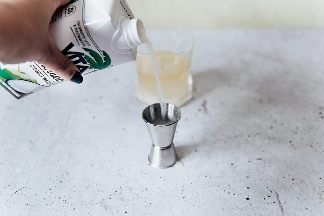 Image of a hand pouring Vita Coco Pressed Coconut Water into a shot to be used in a coconut water drink recipe.