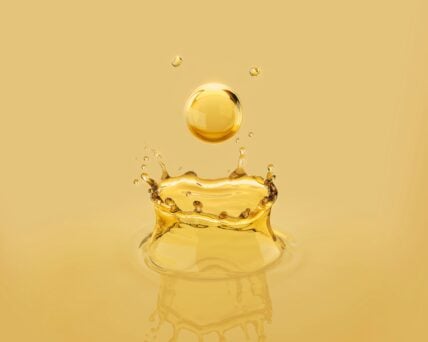 Image of a golden drop of a seed oil dripping and bouncing back into the air.