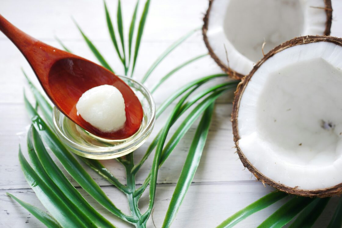 Image of a brown coconut split in half to reveal the white coconut meat within, set next to a glass ramekin with coconut oil and a small red spoon.