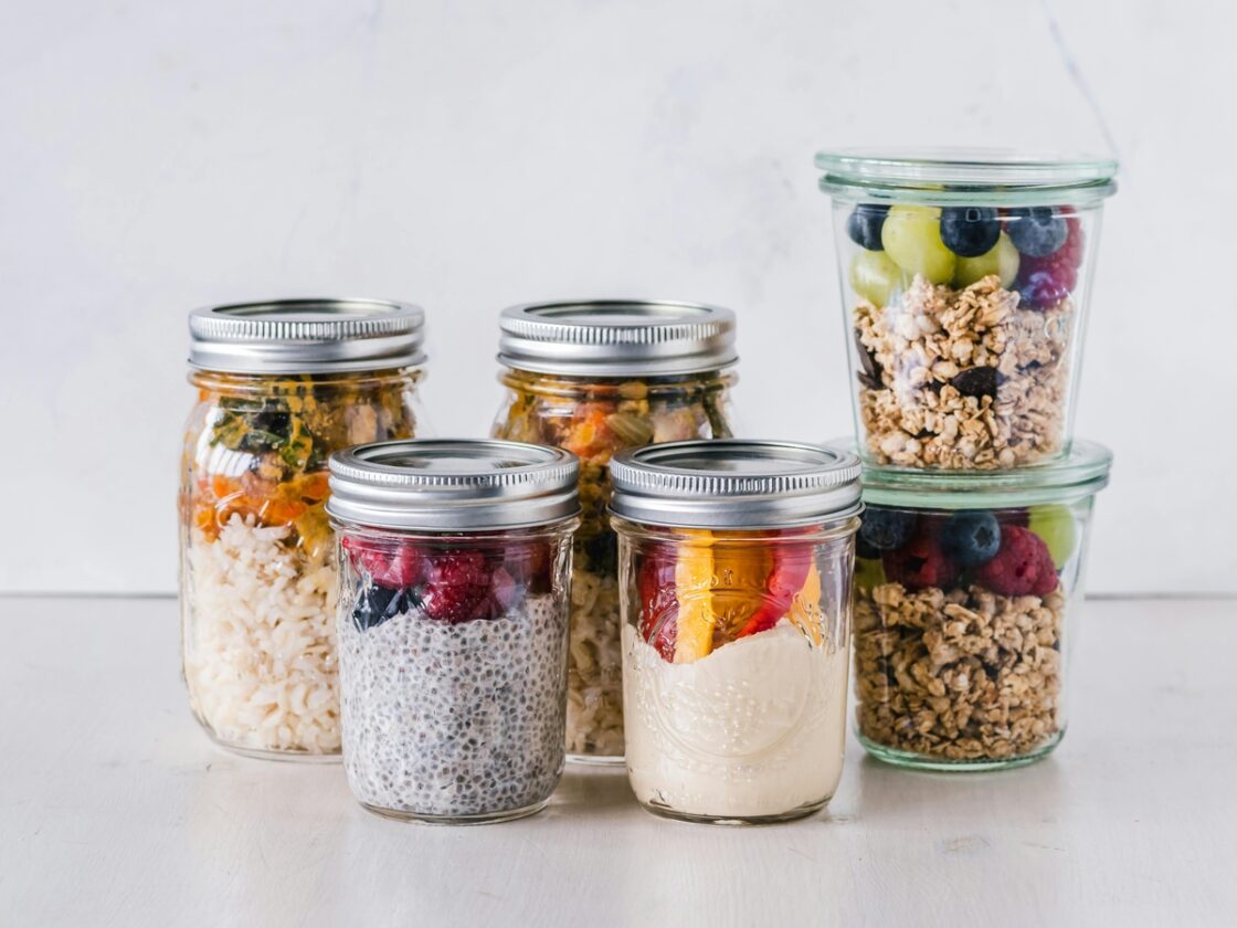 Image of several glass mason jars with silver lids, filled with various fruits, oats, and puddings.