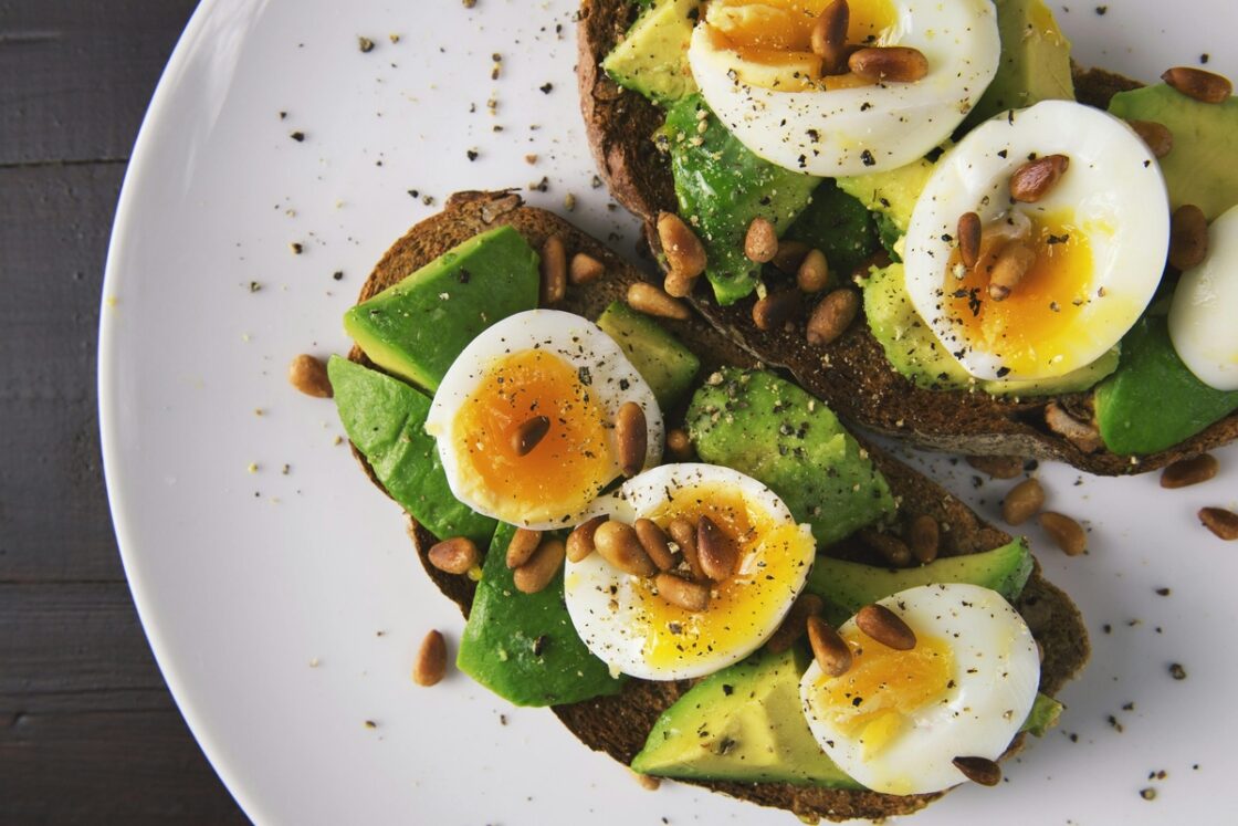 Image of a plate with two slices of rye sourdough toast, topped with slices of avocado and soft boiled eggs.