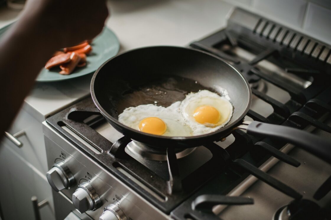 Image of someone cooking two fried eggs in a traditional nonstick pan on a cooktop.