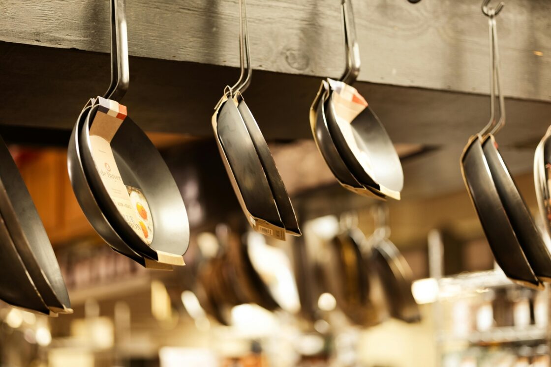 Image of brand new nonstick pans in their packaging hanging from a rail in a kitchen.