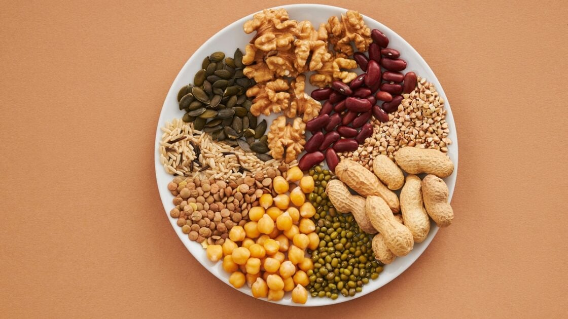 Image of an assortment of nuts, seeds, and beans on a white plate against a brown background.